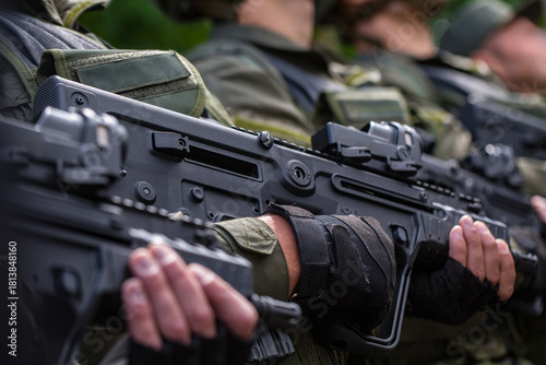 Close up side view of a row of soldiers in green gear holding modern black bullpup assault rifles with red dot collimator sights ready for dangerous military combat defense war operation
