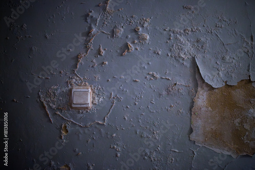 Old weathered blue wall surface with cracked peeling paint and a vintage light switch in a dark abandoned house room creates a spooky mysterious grunge abstract texture background for design