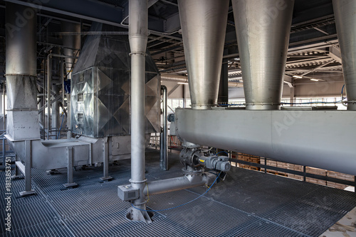 The interior of a modern factory. Large stainless steel hoppers(cyclones) and a screw conveyor(auger) are part of an automated system for conveying bulk powder. The machinery is on a metal grate floor