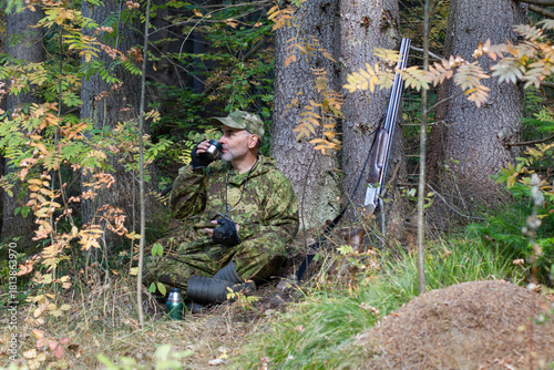 A hunter drinks tea under a tree in the forest