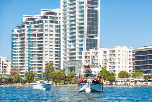 Two boats floating on water with modern apartment buildings in the background in Limassol, Cyprus