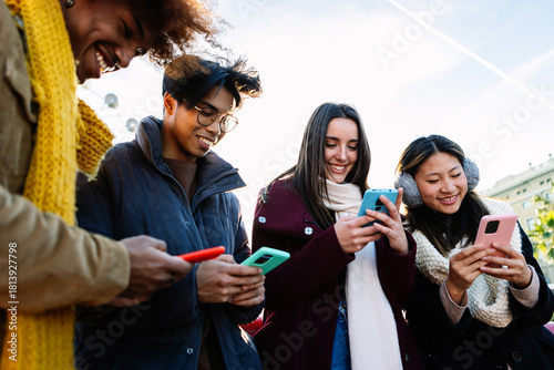 Young group of people in warm clothes using mobile phone device on winter. Social media and technology lifestyle concept