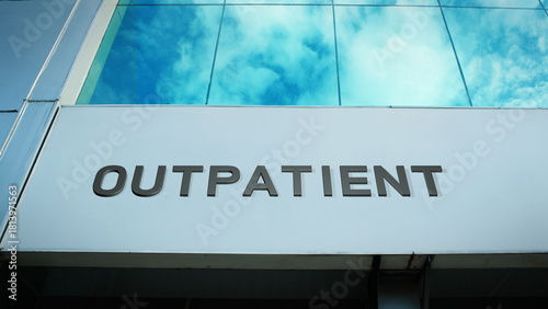 Outpatient sign displayed on a modern glass building with windows reflecting clouds and sky, creating a clean, bright, contemporary exterior with healthcare atmosphere