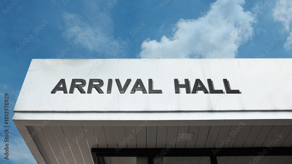 Naklejka premium Arrival Hall word sign displayed on building under clear blue sky, representing airport terminals, travel, passenger services, and public facilities
