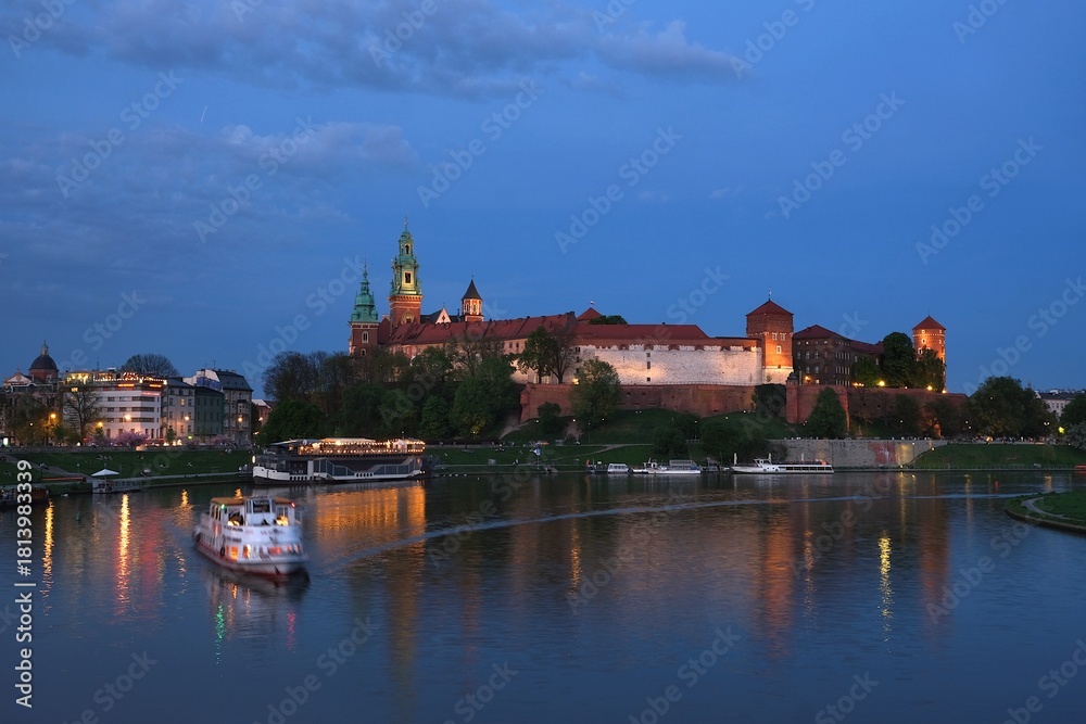 Obraz premium Historic Wawel Castle complex and Vistula River with blurred cruise ship in foreground in night illuminations. Krakow, Poland