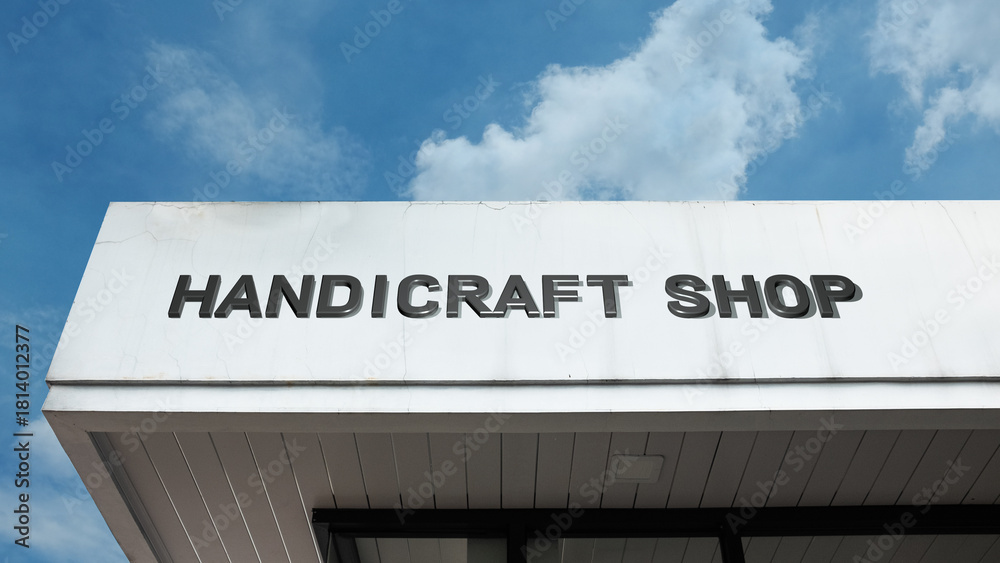 Obraz premium Handicraft Shop sign displayed on a building against a clear blue sky, symbolizing artisanal goods, local craft, retail boutique, creative works, and souvenir store.