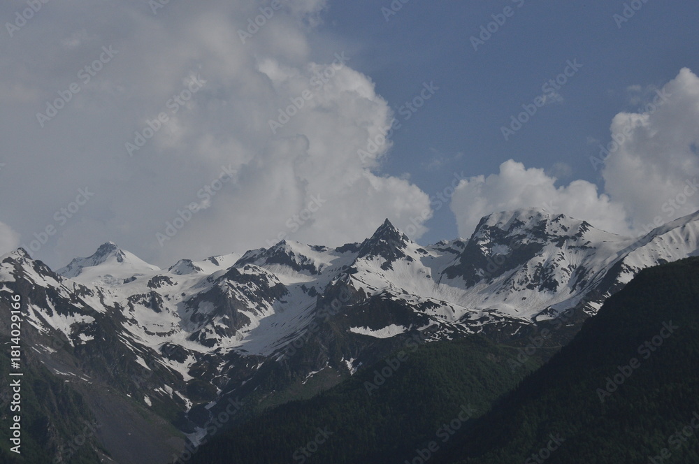 Obraz premium Snow-capped mountain peaks under blue sky with fluffy clouds in the afternoon