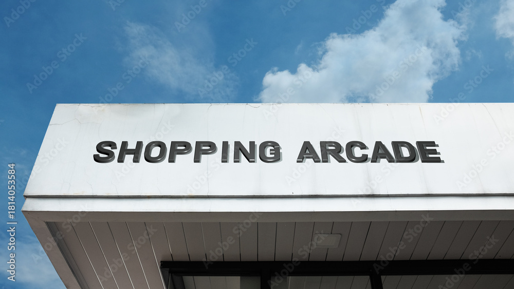 Obraz premium Shopping Arcade word signage on a retail or commercial building under a blue sky, symbolizing multiple stores, enclosed passage, commerce, consumerism, retail complex, and urban marketplace