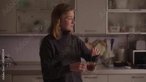 Woman with cerebral palsy stirring tea in double-walled glass mug in kitchen, demonstrating independent daily routine, calm self-care and focused, empowering domestic life. Shooting in slow motion.