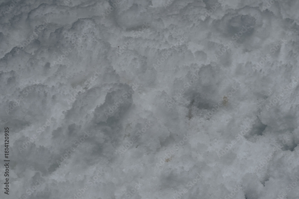 Naklejka premium Detailed close-up view of uneven, rough snow surface showing small mounds, shadows, and natural variations in winter texture and form.