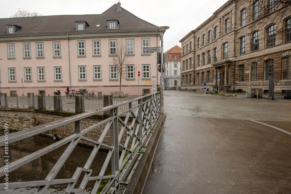 Obraz premium A simple bridge crosses a calm city canal, framed by historic façades and an open square, captured in clear urban space under soft grey daylight.