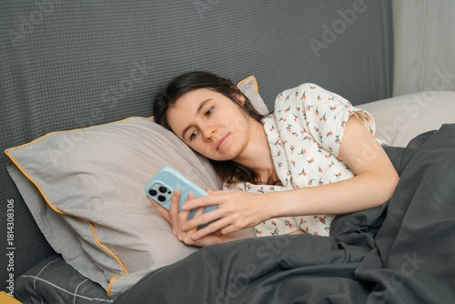 Sick woman lying in bed with smartphone