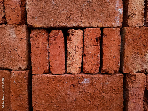 A close-up view of a large, tightly stacked pile of rough red bricks, showcasing the gritty texture and uniform pattern of basic construction materials for a building project.