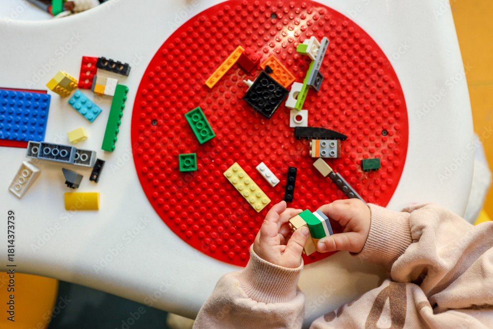 Obraz premium Child's hands playing with colorful building blocks on a red baseplate