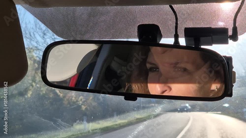 Driving woman road trip. Female reflection visible in car rearview mirror while traveling the highway on a sunny day.