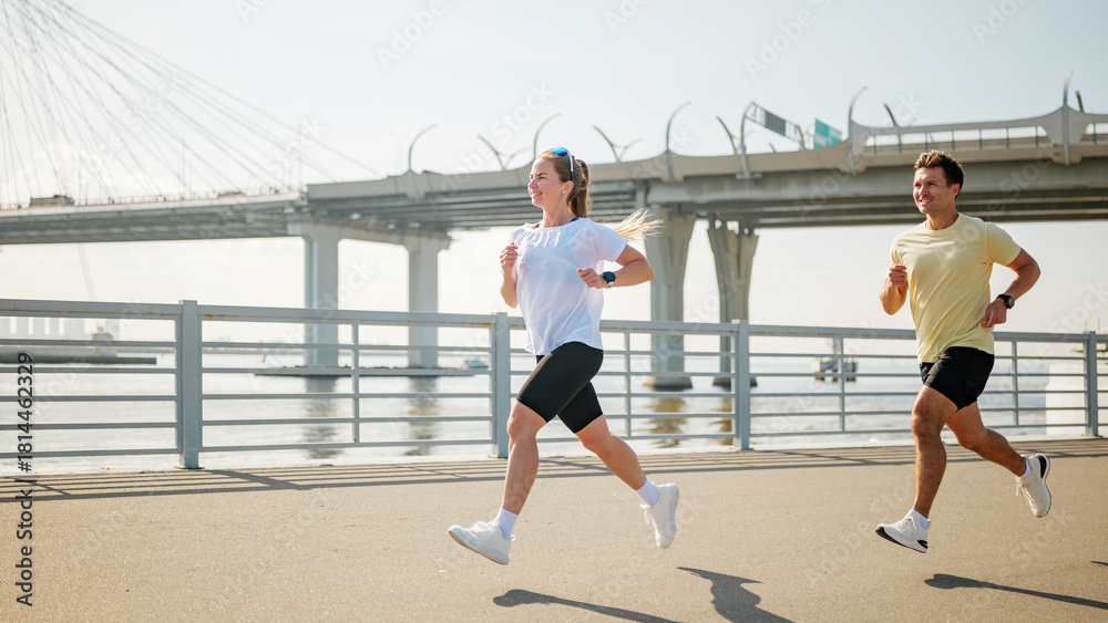 Fototapeta premium Couple running along riverside path in sunny weather