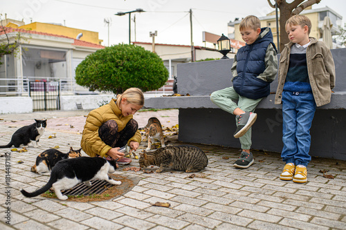 Children feeding stray cats outdoors, sharing food with homeless animals in a warm and candid moment of kindness and compassion on a quiet street.