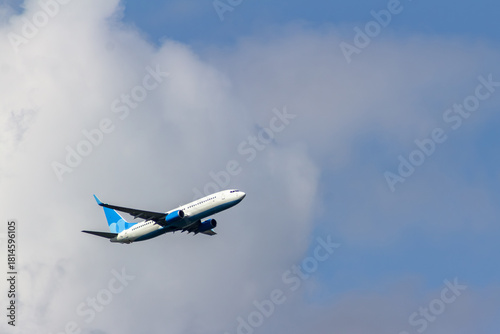 Fotografie Passenger airliner in white and blue colors taking off against a blue sky with clouds