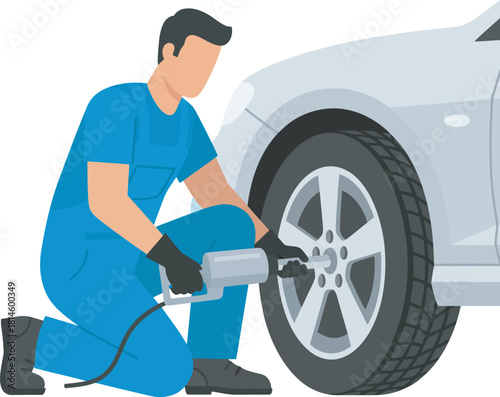 A mechanic in blue overalls kneels, using a tool to change a car tire.