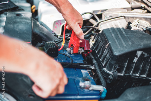 Under the hood of the car, the mechanic connects the clamp of the car jump starter to the terminal of the dead car battery