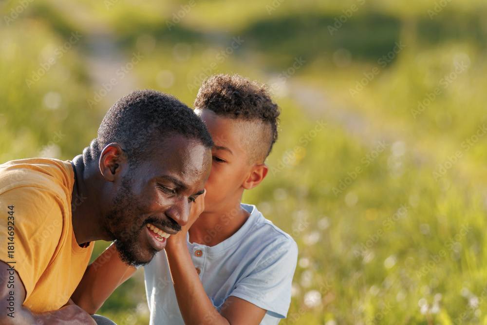 Fototapeta premium Moment of connection, boy sharing secrets with a father, whispering to him in his ear while enjoying playing time together in nature.