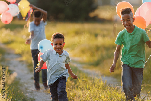 African American children enjoying a joyful day in nature, running with colorful balloons along a rural path near green meadows at summer sunset.