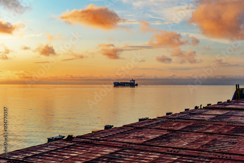 Editorial. 1 July 2025 Baltic Sea. Container ship at sea during a calm sunset, viewed from another vessel. Soft golden light, gentle waves and distant cargo vessel create a peaceful maritime scene.