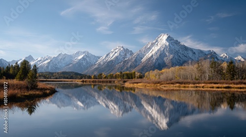 Landscape photograph of a mountain range reflected in a calm lake. the mountains are covered in snow and the sky is blue with a few scattered clouds.
