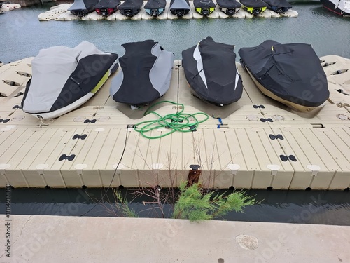Jet skis covered and secured on a pier with calm water and boat docks in the background