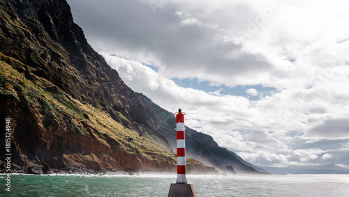 Coastal lighthouse standing on rocky shore, surrounded by ocean waves and cliffs, under a dramatic sky with clouds, symbolizing guidance and safety in maritime navigation