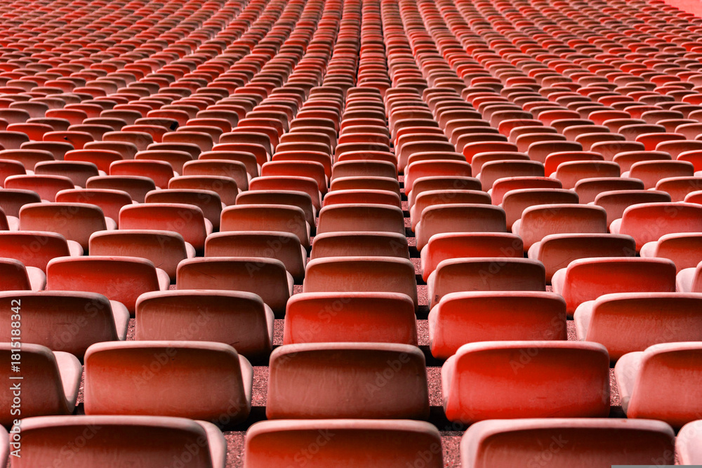 Fototapeta premium Wide view of rows of empty red stadium seats forming a strong repetitive and symmetrical pattern. Clean sports arena seating background ideal for football and soccer concepts, sports events, audience 