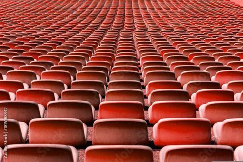 Wide view of rows of empty red stadium seats forming a strong repetitive and symmetrical pattern. Clean sports arena seating background ideal for football and soccer concepts, sports events, audience 