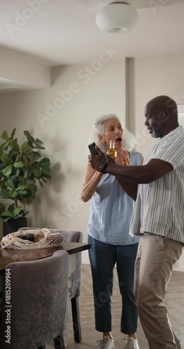Vertical video: Unpacking bag sparking diverse senior couple dancing with olive oil jar by table