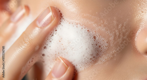A close-up view of a person gently massaging a foamy cleanser onto their cheek, part of a daily skincare routine for healthy, clean skin