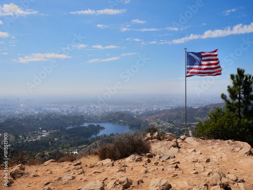 Flag of the United States of America waving on Cahuenga Peak at Wisdom Tree with the Hollywood Reservoir and skyline of LA in the background during a summer season in Los Angeles, California, USA