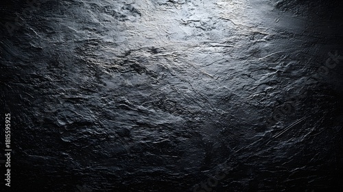 Dramatic spotlight illuminates rugged dark stone surface texture with deep shadows