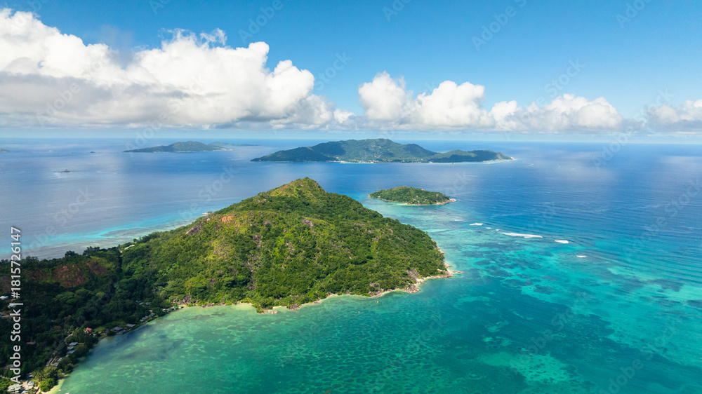 Fototapeta premium Aerial view of island with dense green vegetation sits amidst the turquoise waters. Praslin, Seychelles.