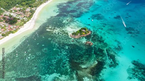 фотографія A small, lush island sits in shallow turquoise waters, surrounded by coral reefs and close to a white sandy shore