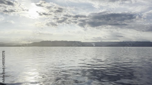 Tranquil Serenity: Calm Waters Reflecting Sunlight Amidst Majestic Mountains and Fluffy Clouds. HDR Video, Seamless Loop