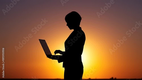 Silhouette of a person working on a laptop against a vibrant sunset sky, symbolizing remote work