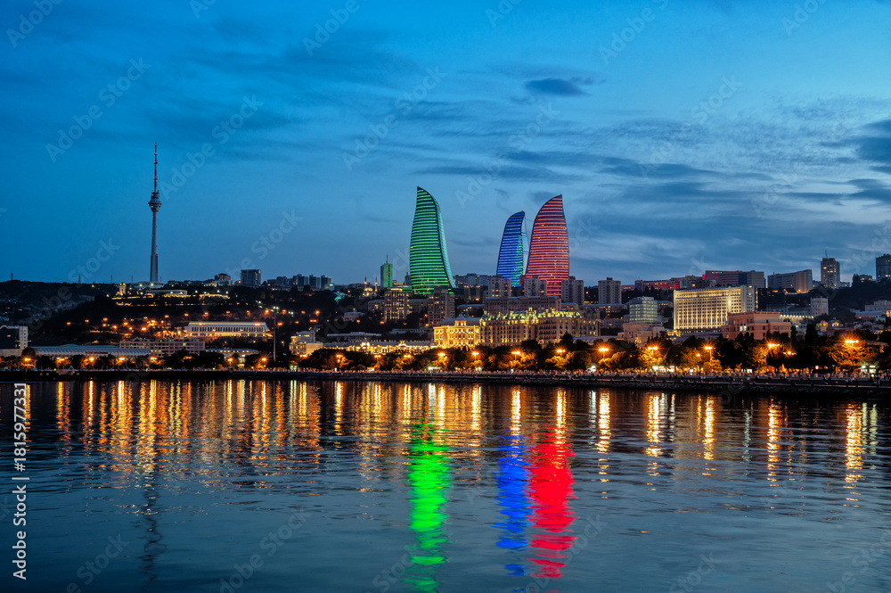 Fototapeta premium Baku skyline at blue hour with illuminated towers reflecting on the water, captured at dusk in Azerbaijan.