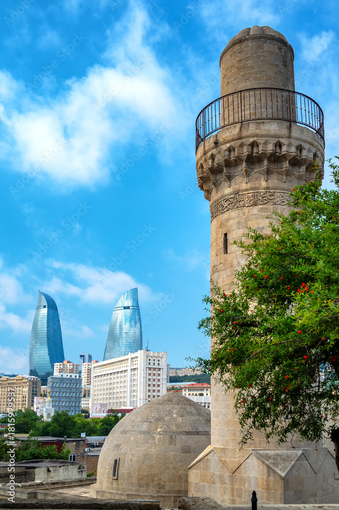 Fototapeta premium Vertical view of the Shirvanshah Palace Mosque in Baku Azerbaijan with domes and minaret framed by modern skyscrapers under a bright blue sky.