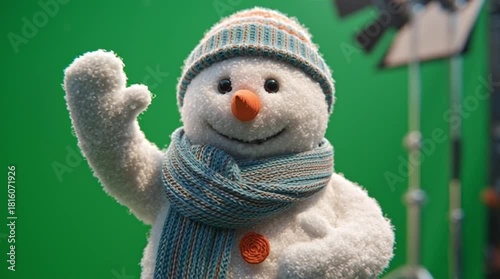 A cheerful snowman with a striped hat and scarf waves hello on a vibrant green screen background, perfect for holiday designs