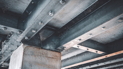 Close-up of an industrial structure featuring robust steel beams, cross-members, and a concrete support column, all secured with numerous bolts from below.