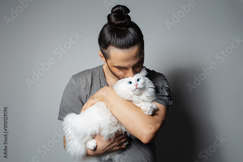 Bilde på lerret Studio portrait of young man with white cat in arms while kissing the pet on grey background