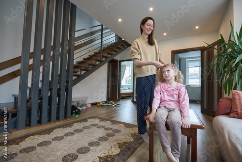 Quadro su tela Mother braiding daughter's hair in modern home interior with wooden staircase