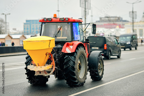 Salt spreading tractor. Winter maintenance tractor spreading salt mixture along city road to improve traction and prevent accidents caused by snow and ice accumulation, urban road deicing operation
