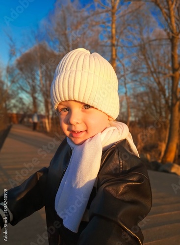 A 3-year-old little boy on a walk in autumn wearing a white hat and scarf