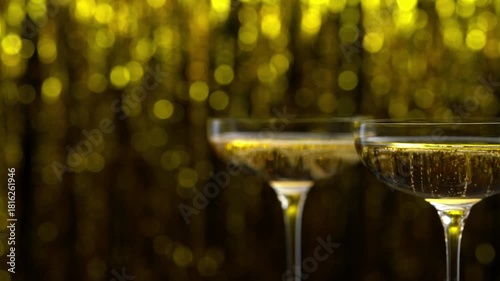Two coupe glasses of champagne on golden bokeh background. Champagne in a two coupe glases on a table. Glasses with champagne placed on a table.