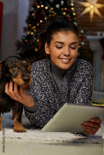 Woman shopping online at home in Winter. Happy young woman lying on floor using tablet and bank card for online shopping at home at Christmas time. Christmas tree and fireplace in background.